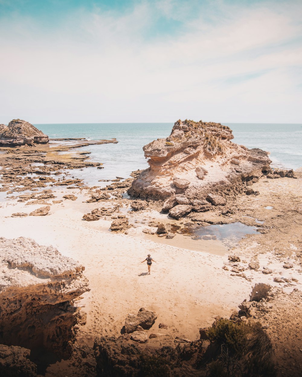 Persona parada en una formación rocosa marrón cerca del cuerpo de agua durante el día
