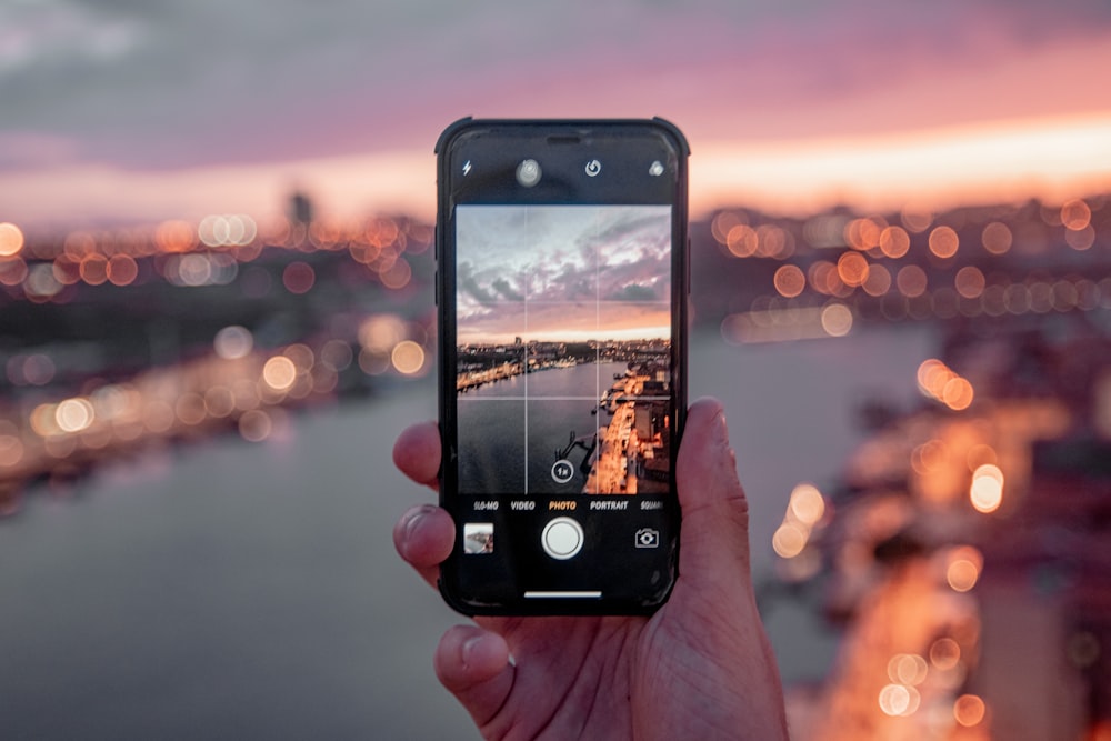Personne tenant un iPhone 5 noir prenant une photo de la ville au coucher du soleil