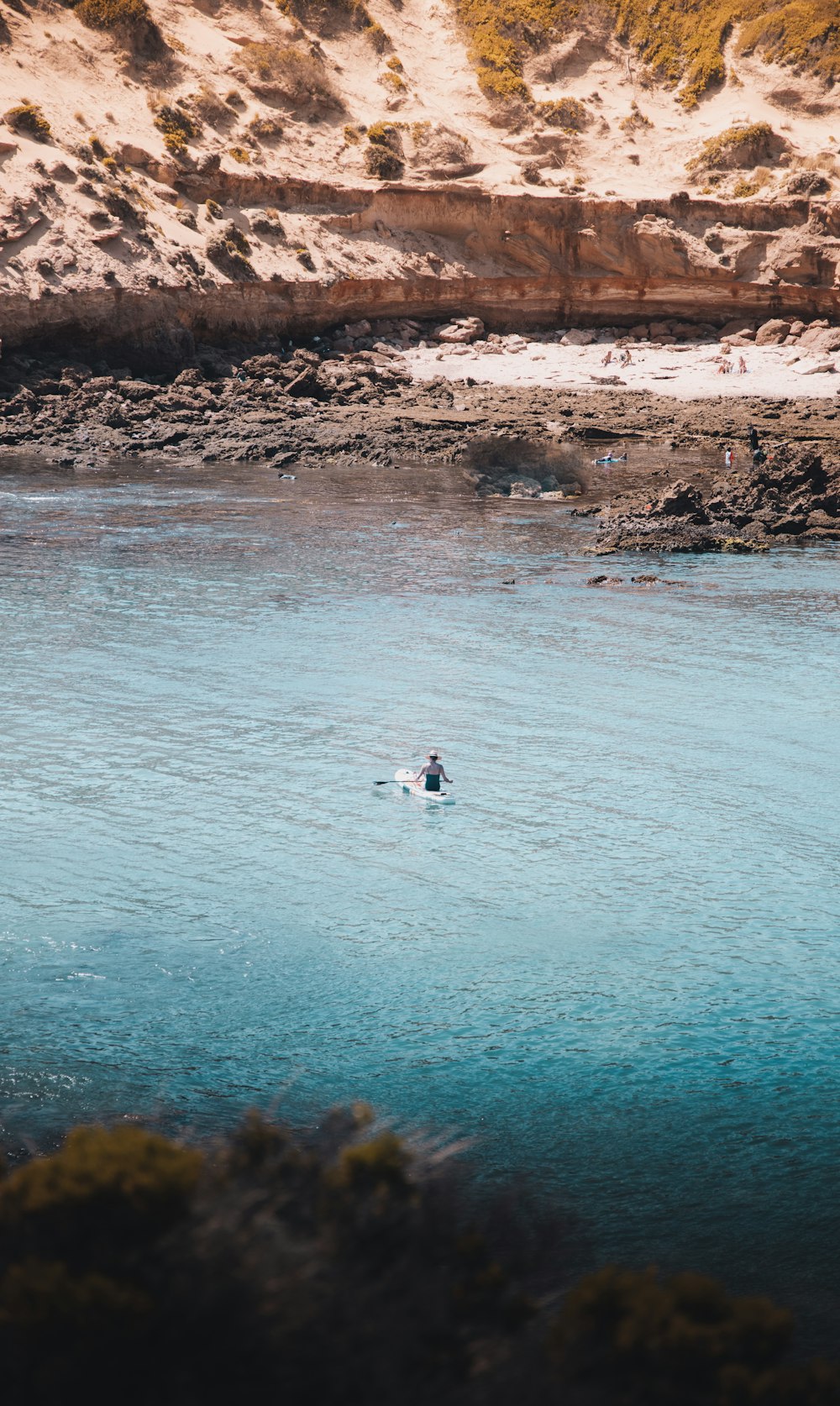 person in white shirt and black pants sitting on white surfboard on body of water during