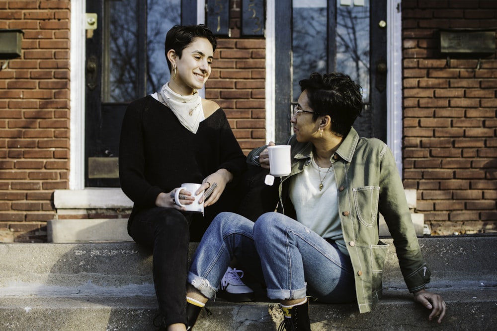 woman in black sweater and blue denim jeans sitting beside woman in brown coat