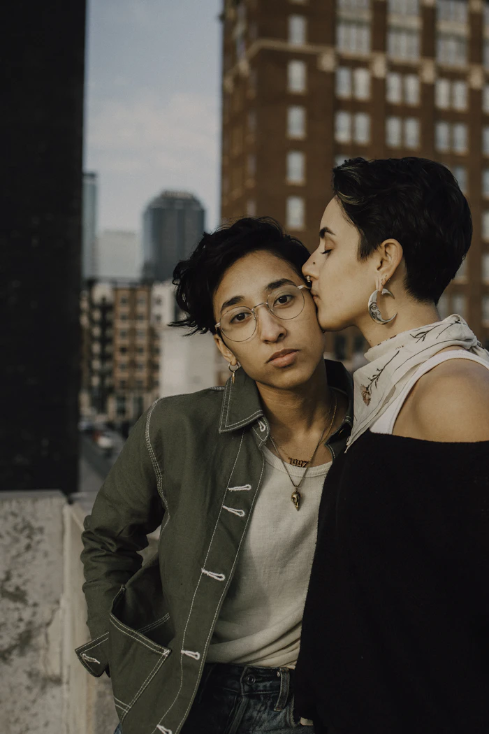 Marisol kissing Jo on the cheek with city towers behind them