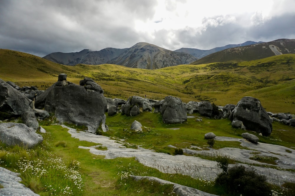 roches grises sur le champ d’herbe verte près de la montagne sous les nuages blancs pendant la journée
