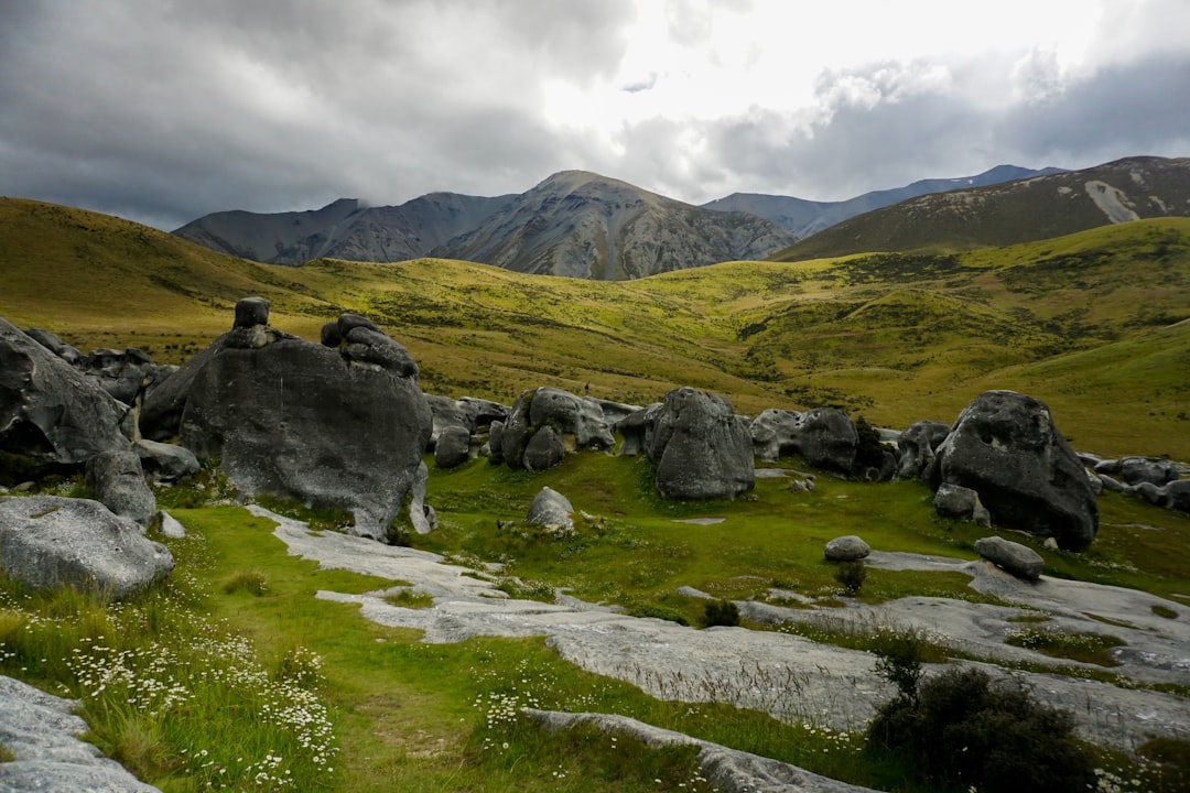 gray rocks on green grass field near mountain under white clouds during daytime