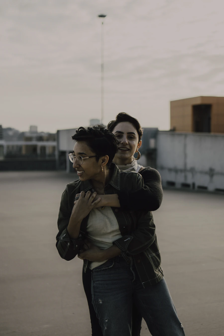 Marisol hugging Jo from behind on the rooftop at golden hour