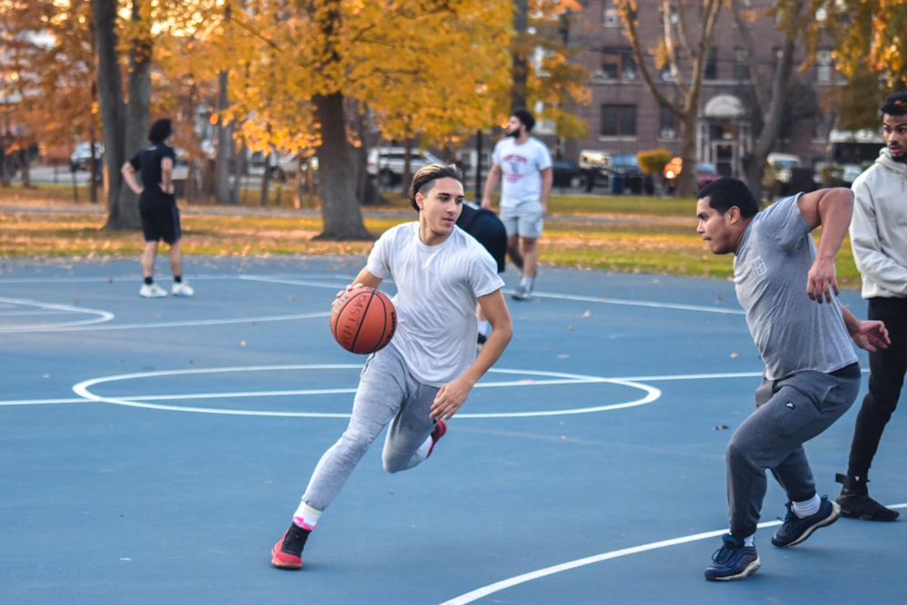 Hombre con camiseta blanca de cuello redondo Nike y pantalones grises jugando baloncesto durante el día