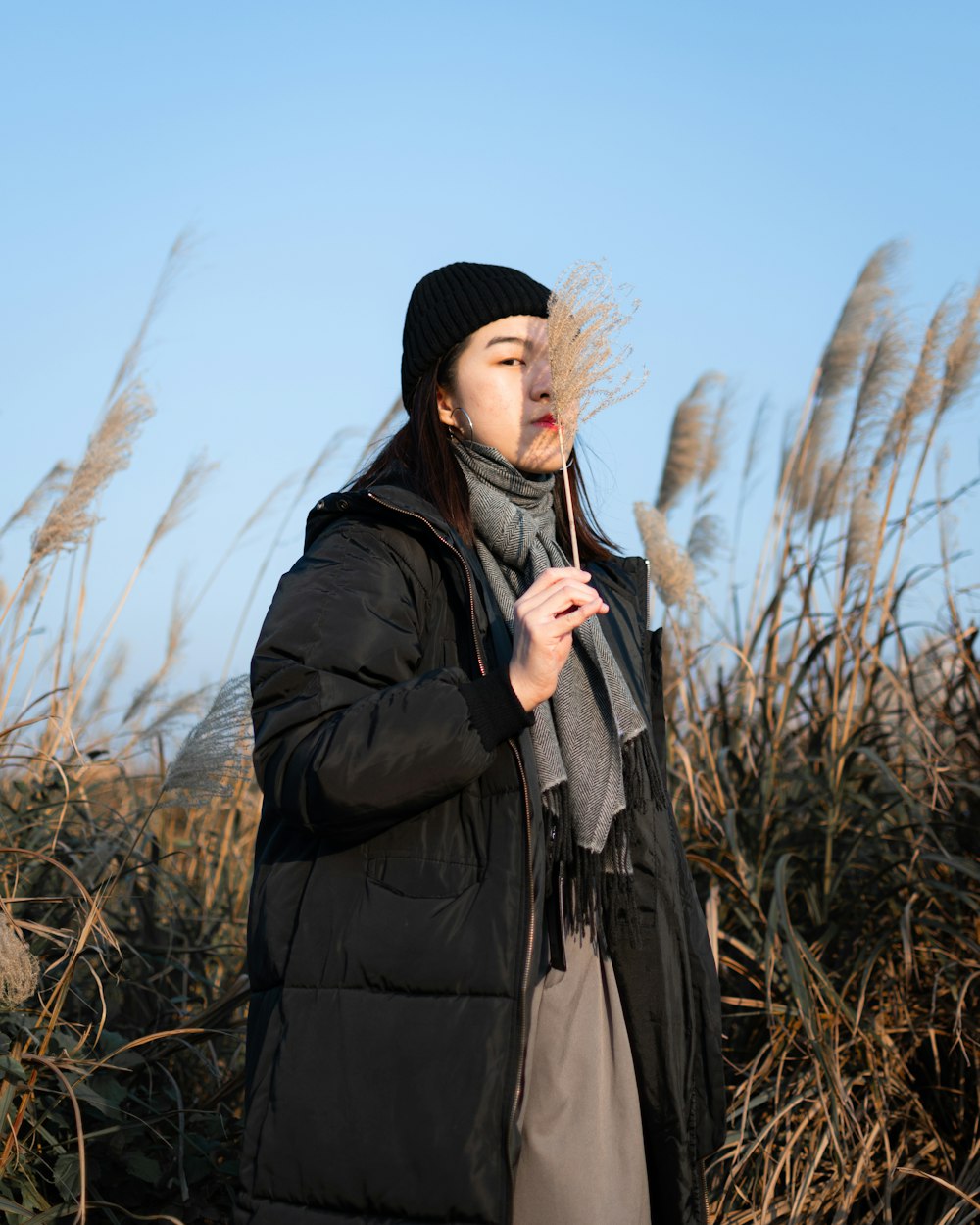 woman in black knit cap and black jacket standing on brown grass field during daytime