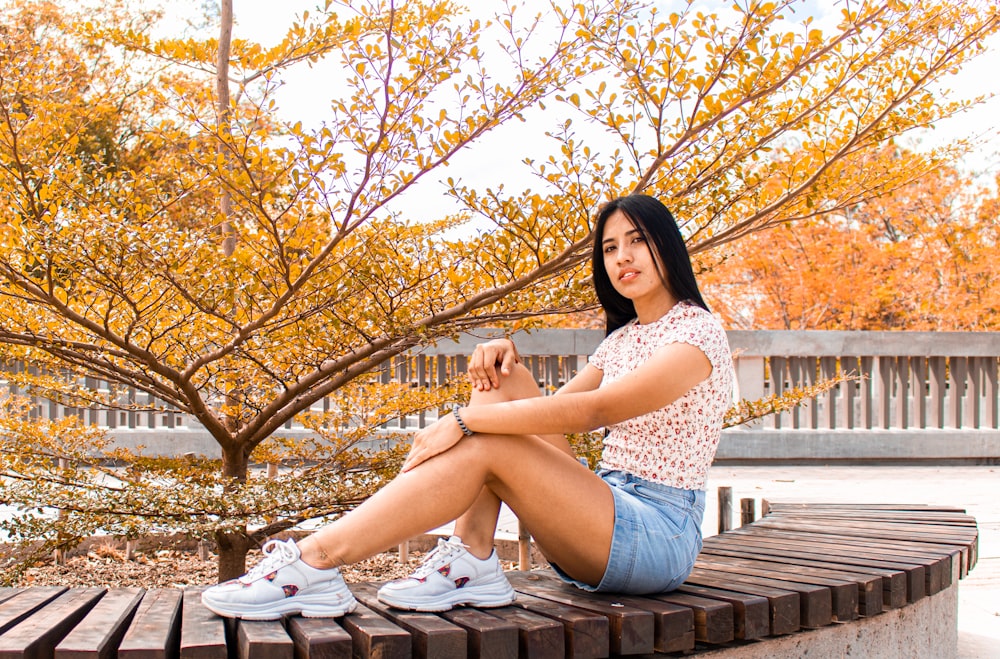 woman in white and black floral tank top and blue denim shorts sitting on brown wooden