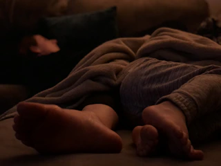 A cozy pair of cotton slippers resting beside a warm, knitted blanket on a sunlit wooden floor.
