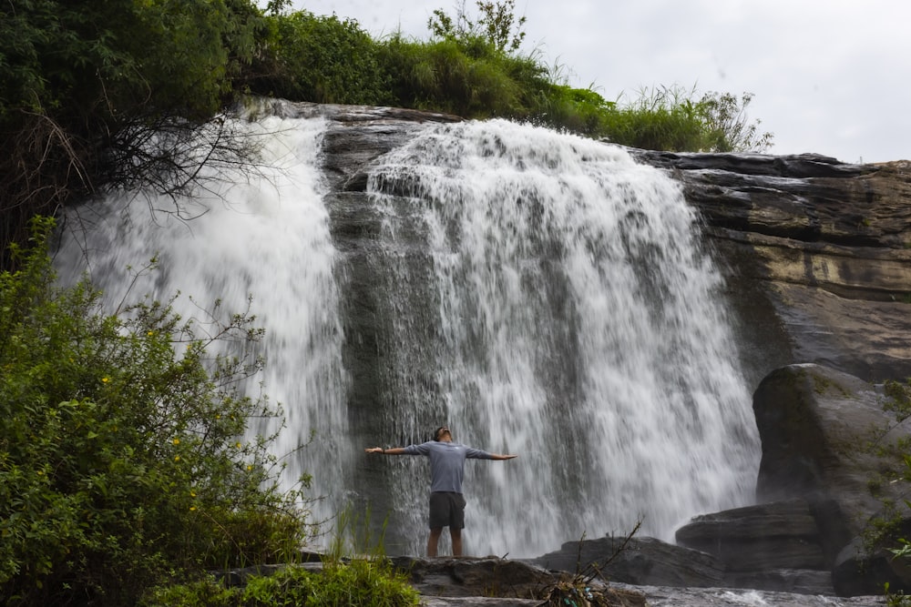 man in brown shirt standing on rock near waterfalls during daytime