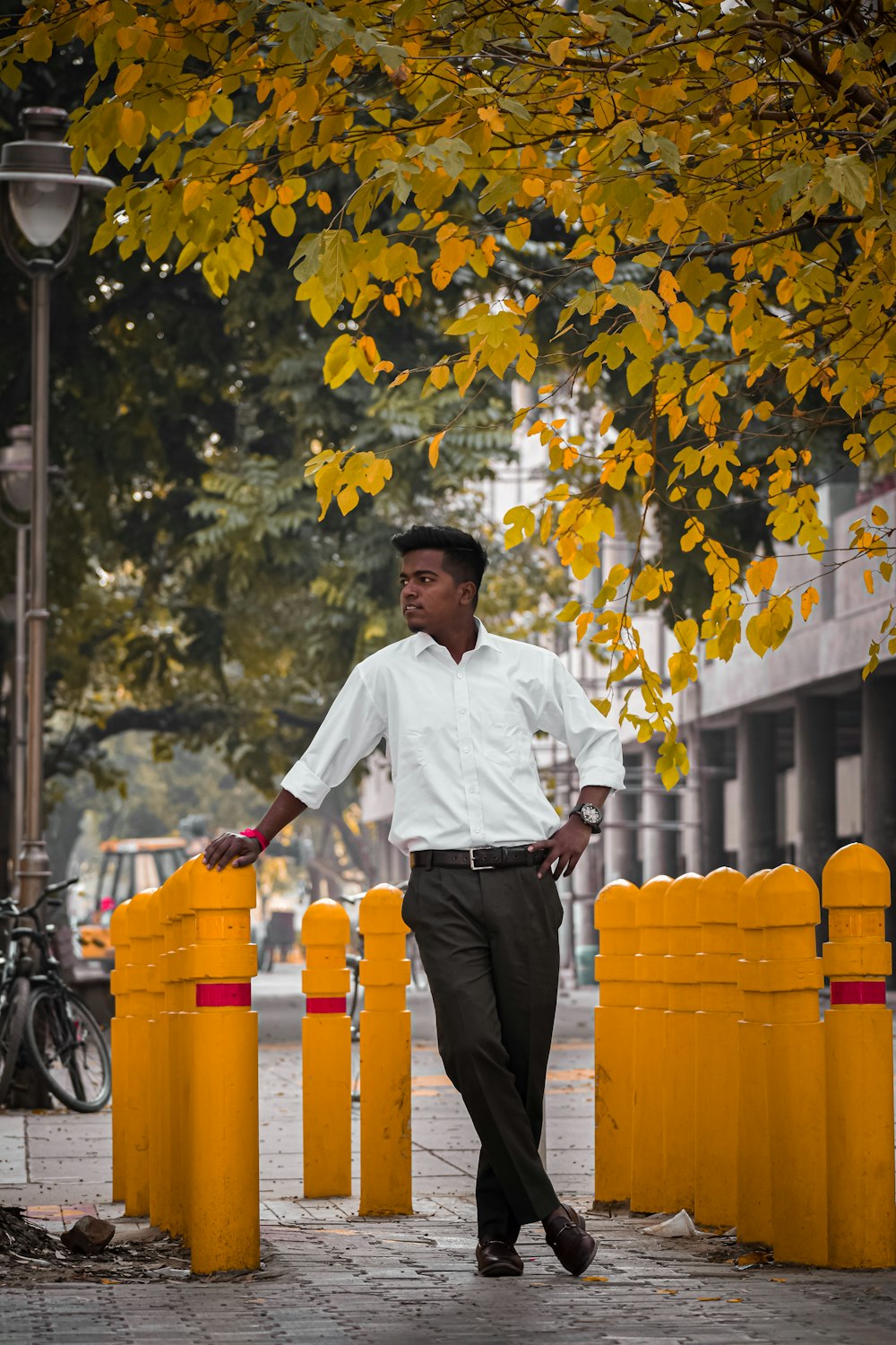 man in white dress shirt and black pants standing near yellow plastic trash bins during daytime