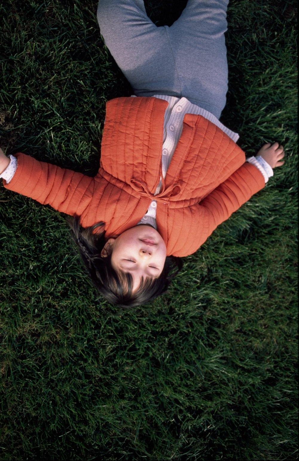 woman in red and gray sweater lying on green grass