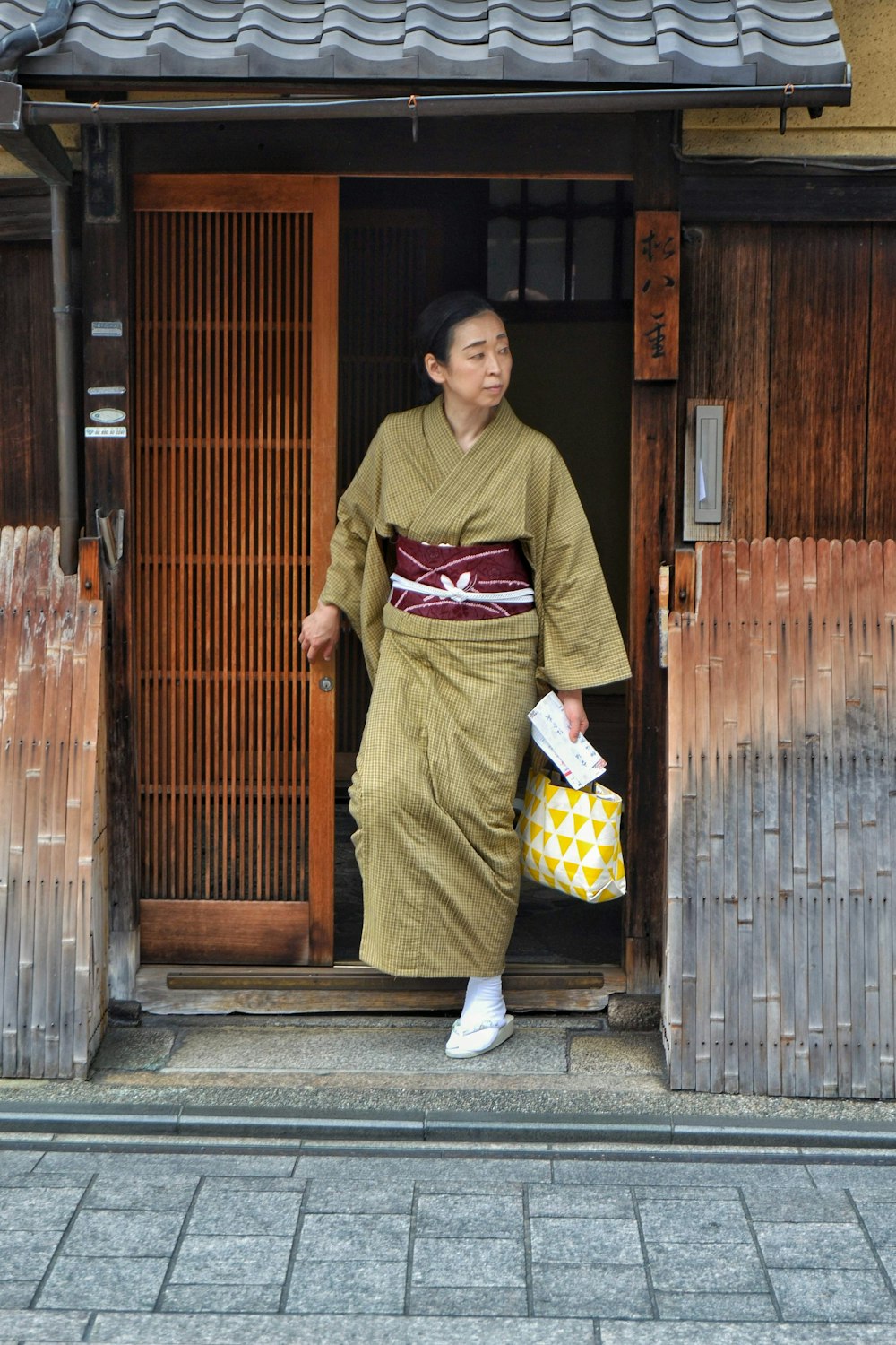 Frau im grün-gelben Kimono neben brauner Holztür