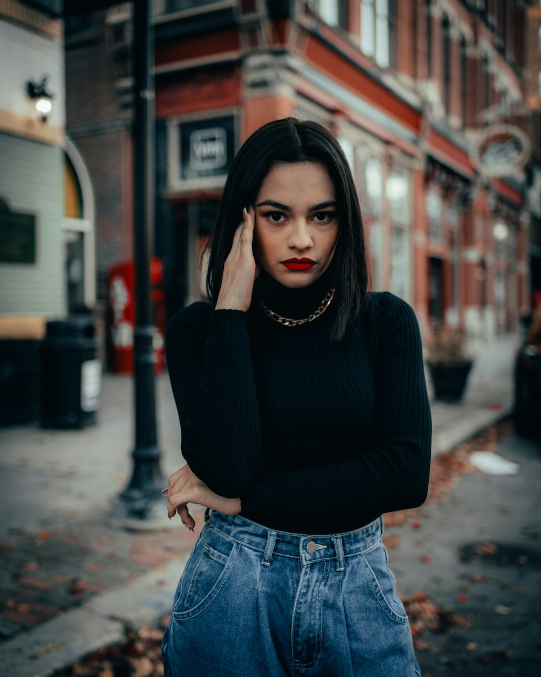 woman in black long sleeve shirt and blue denim jeans standing on sidewalk during daytime