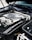 The image features the engine bay of a high-performance vehicle, showcasing a clean and well-maintained engine. Prominent branding includes an AMG logo on the engine cover, suggesting it is a Mercedes-AMG engine. The metallic components are arranged neatly, with visible pipes, wires, and textured areas.