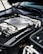 The image features the engine bay of a high-performance vehicle, showcasing a clean and well-maintained engine. Prominent branding includes an AMG logo on the engine cover, suggesting it is a Mercedes-AMG engine. The metallic components are arranged neatly, with visible pipes, wires, and textured areas.