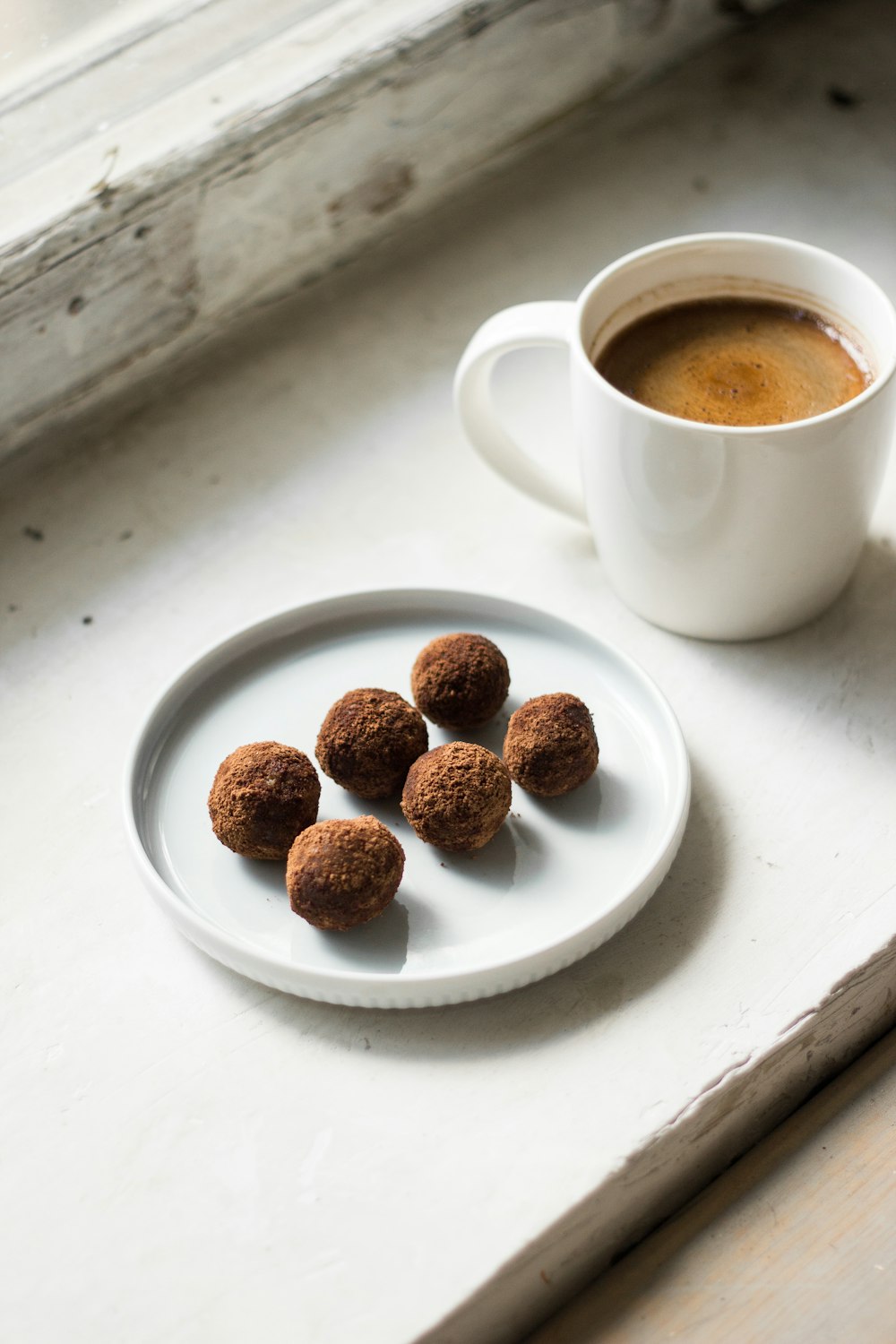 a cup of coffee next to a plate of chocolate truffles
