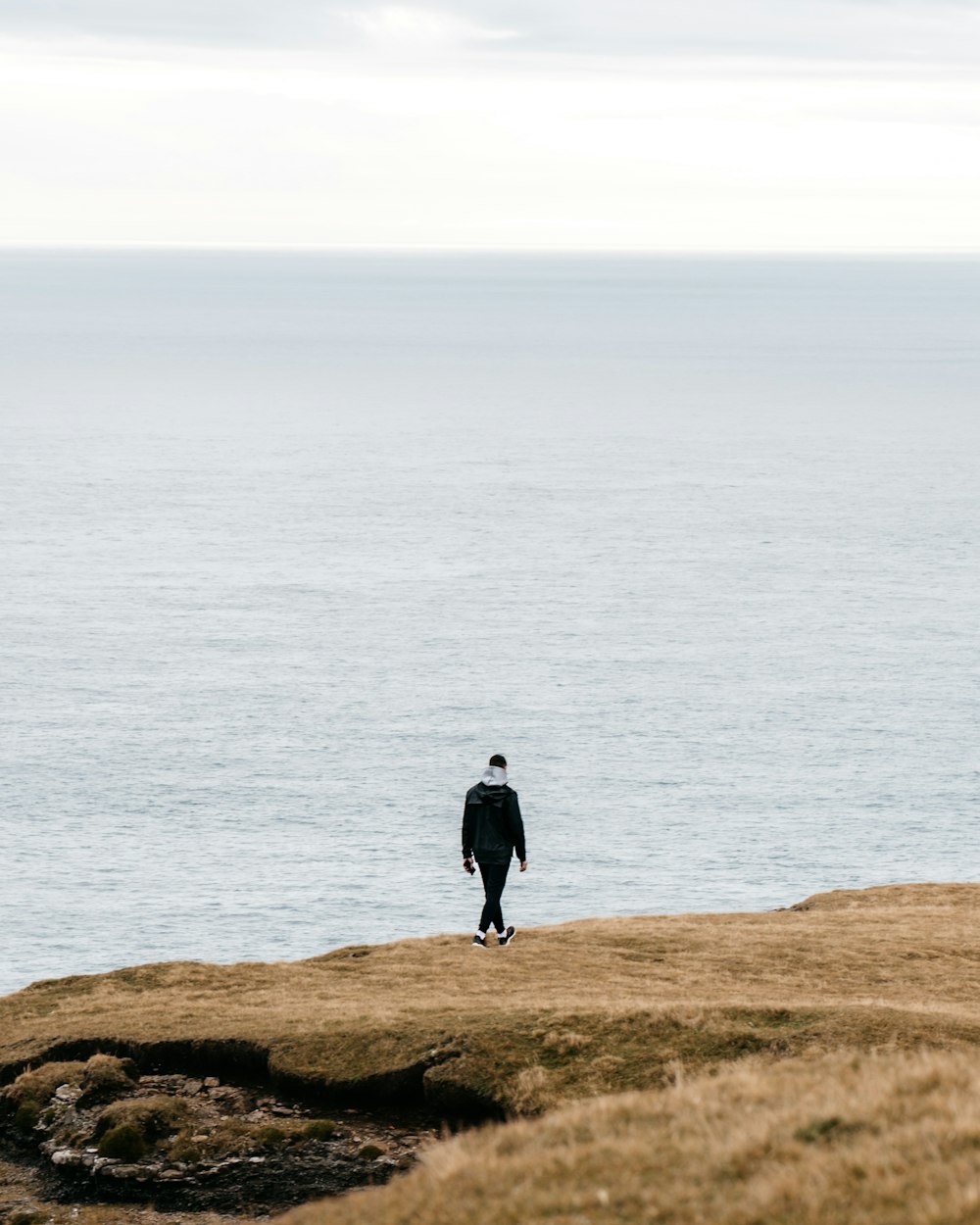 man in black jacket standing on brown rock near body of water during daytime