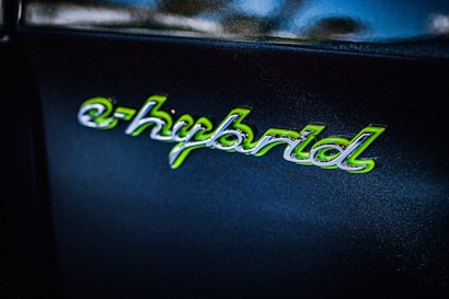 The image shows the word 'e-hybrid' written in a stylized script with green accents on a dark background. The text appears glossy and reflective, suggesting it is part of a logo or badge, possibly on a vehicle.