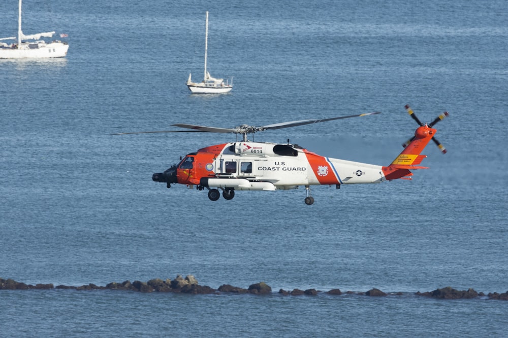 낮 동안 물의 시체에 흰색과 주황색 헬리콥터