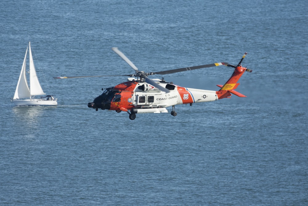낮에는 바다 위를 날아다니는 주황색과 흰색 헬리콥터