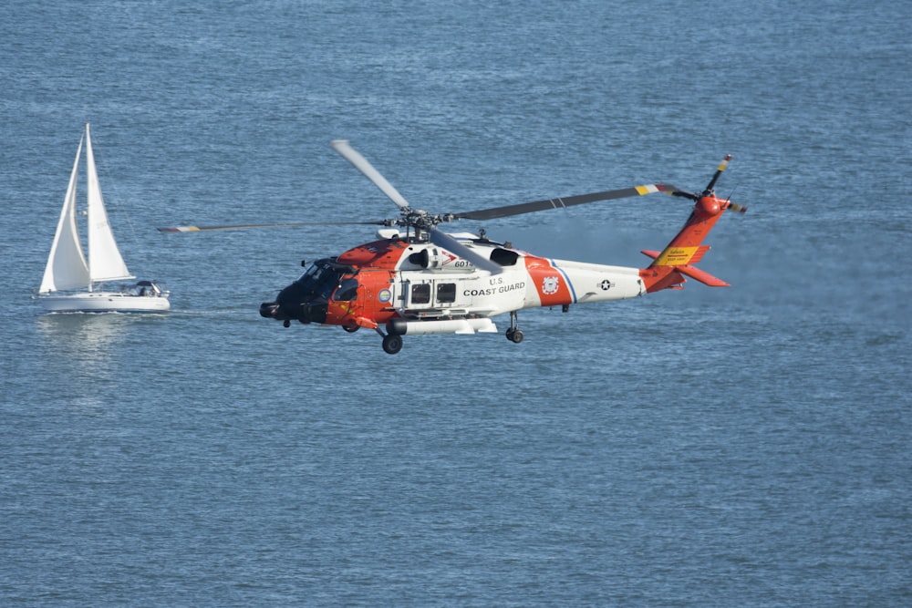 elicottero arancione e bianco che sorvola il mare durante il giorno