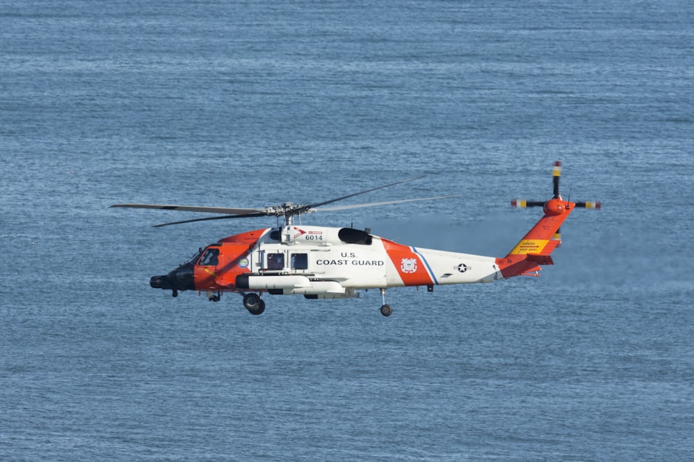 weißer und orangefarbener Hubschrauber, der tagsüber über das Meer fliegt