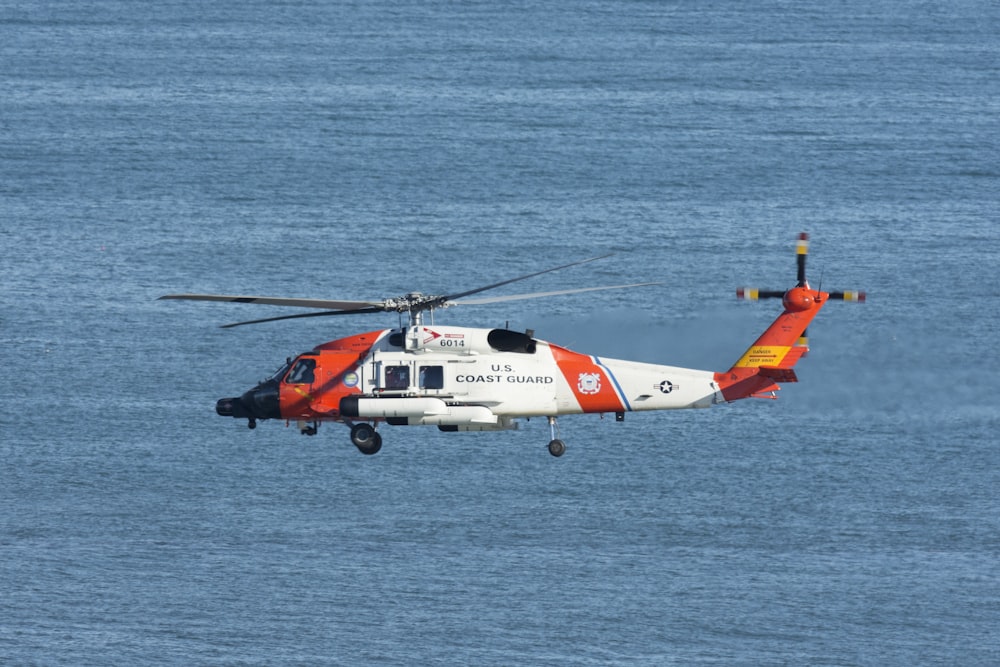 낮 동안 바다 위를 비행하는 흰색과 주황색 헬리콥터