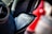A close-up of a car's speaker system, focusing on the Bowers & Wilkins speaker integrated into a plush black interior with red stitching. A ventilation grille is visible to the left, and there is a blurred red object in the background suggesting a vibrant and modern car interior.
