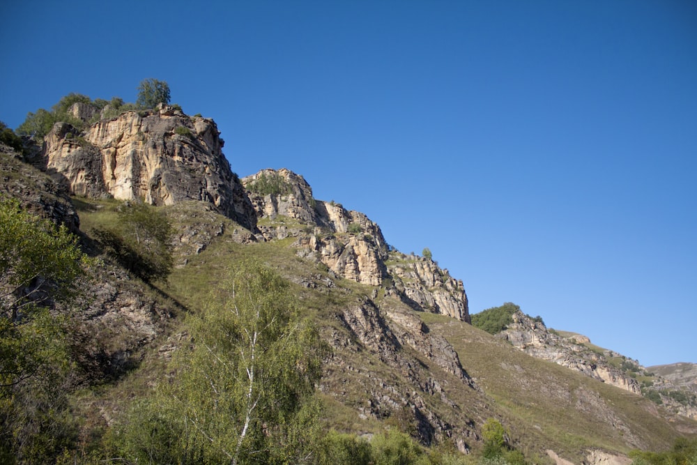 grama verde na montanha rochosa sob o céu azul durante o dia