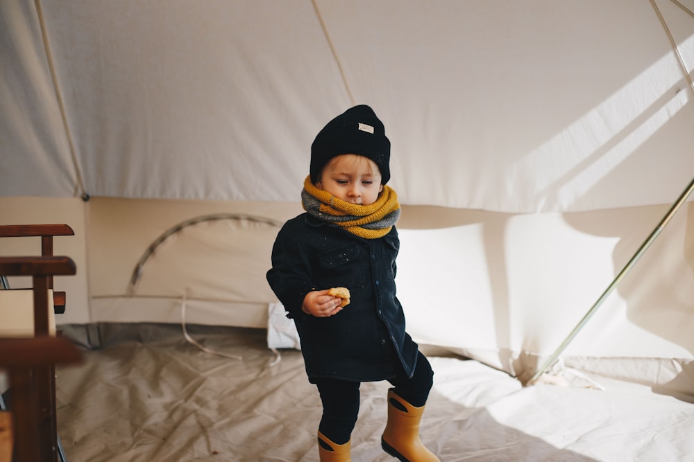 child in black and yellow hoodie standing on white textile