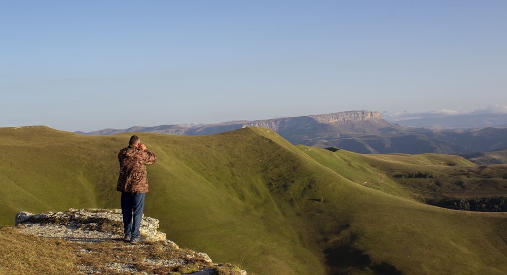 man in brown jacket standing on rock formation during daytime