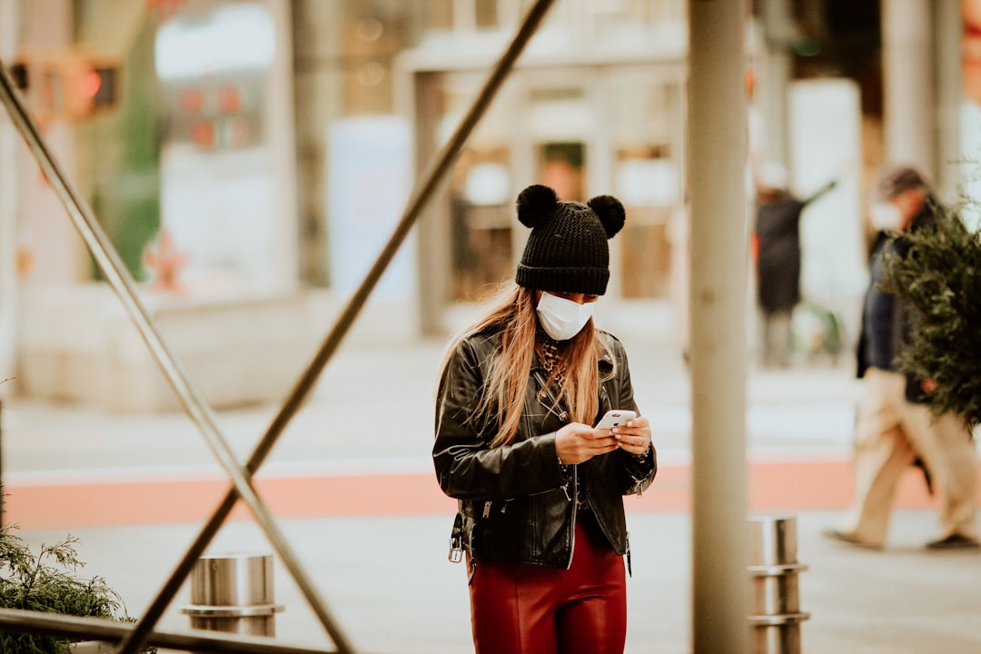 woman in black leather jacket and red pants wearing black hat standing near brown wooden railings