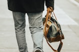 A man carrying a zarvion leather laptop bag while walking through a city street.