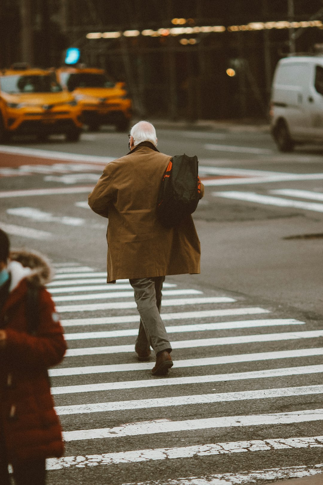 woman in brown coat and blue denim jeans walking on pedestrian lane during daytime