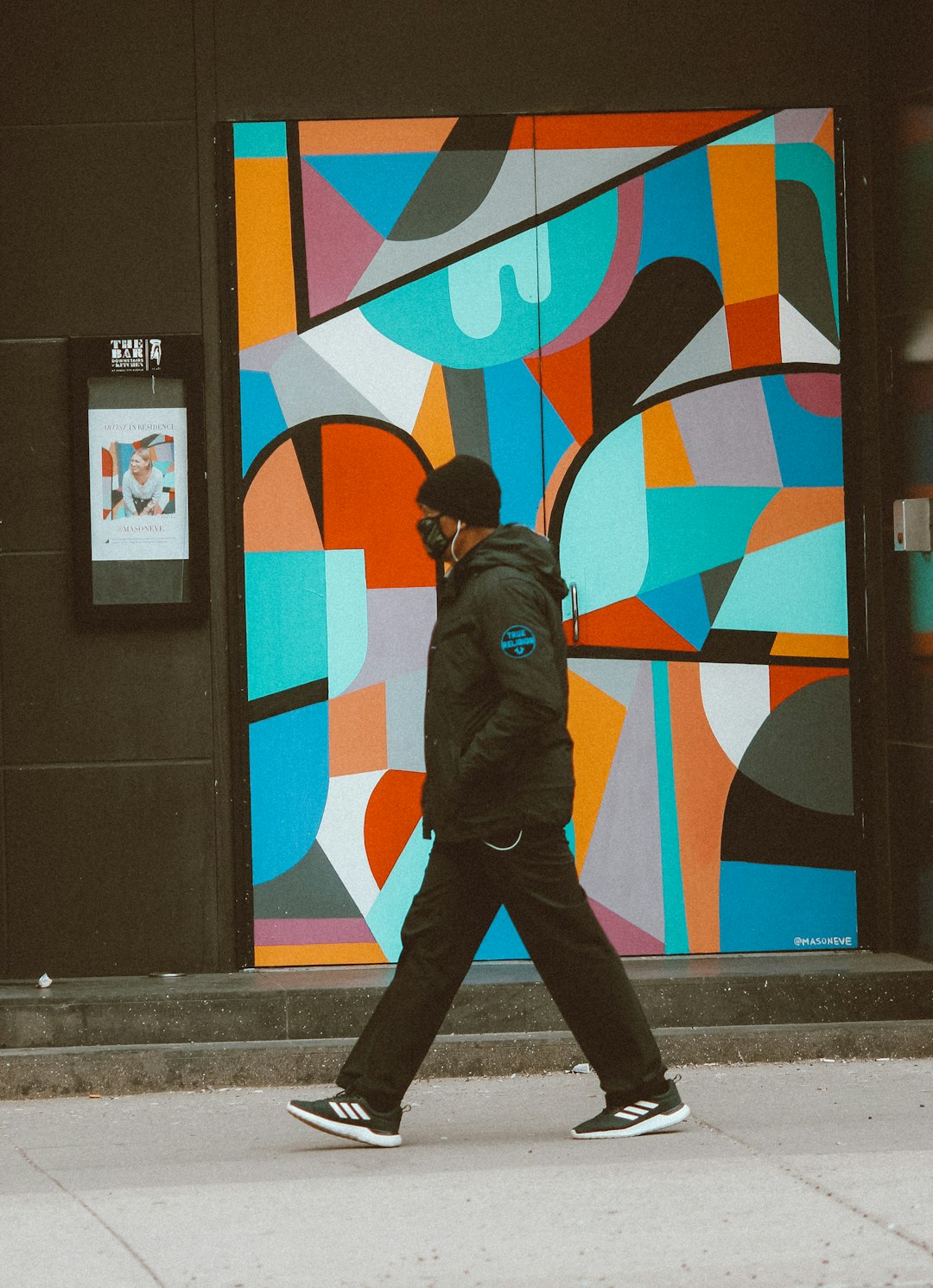 man in brown jacket and black pants standing beside wall with graffiti