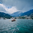 boat on sea near mountain under white clouds and blue sky during daytime