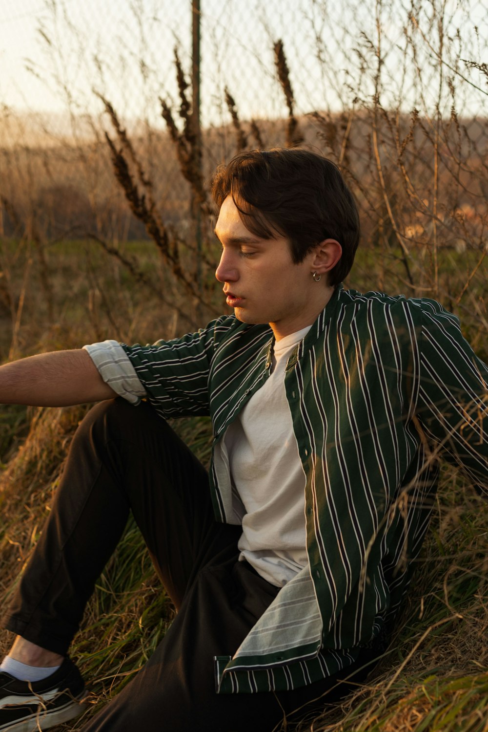 man in black and white striped dress shirt sitting on brown grass field during daytime