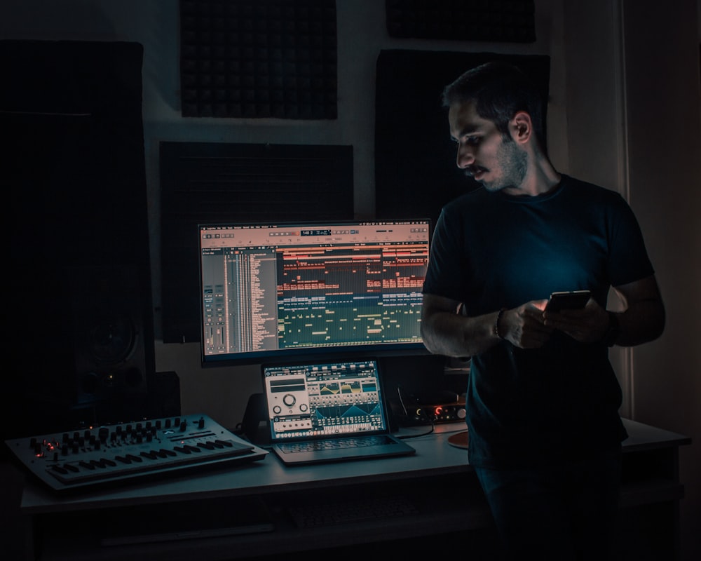 man in blue crew neck t-shirt standing beside computer