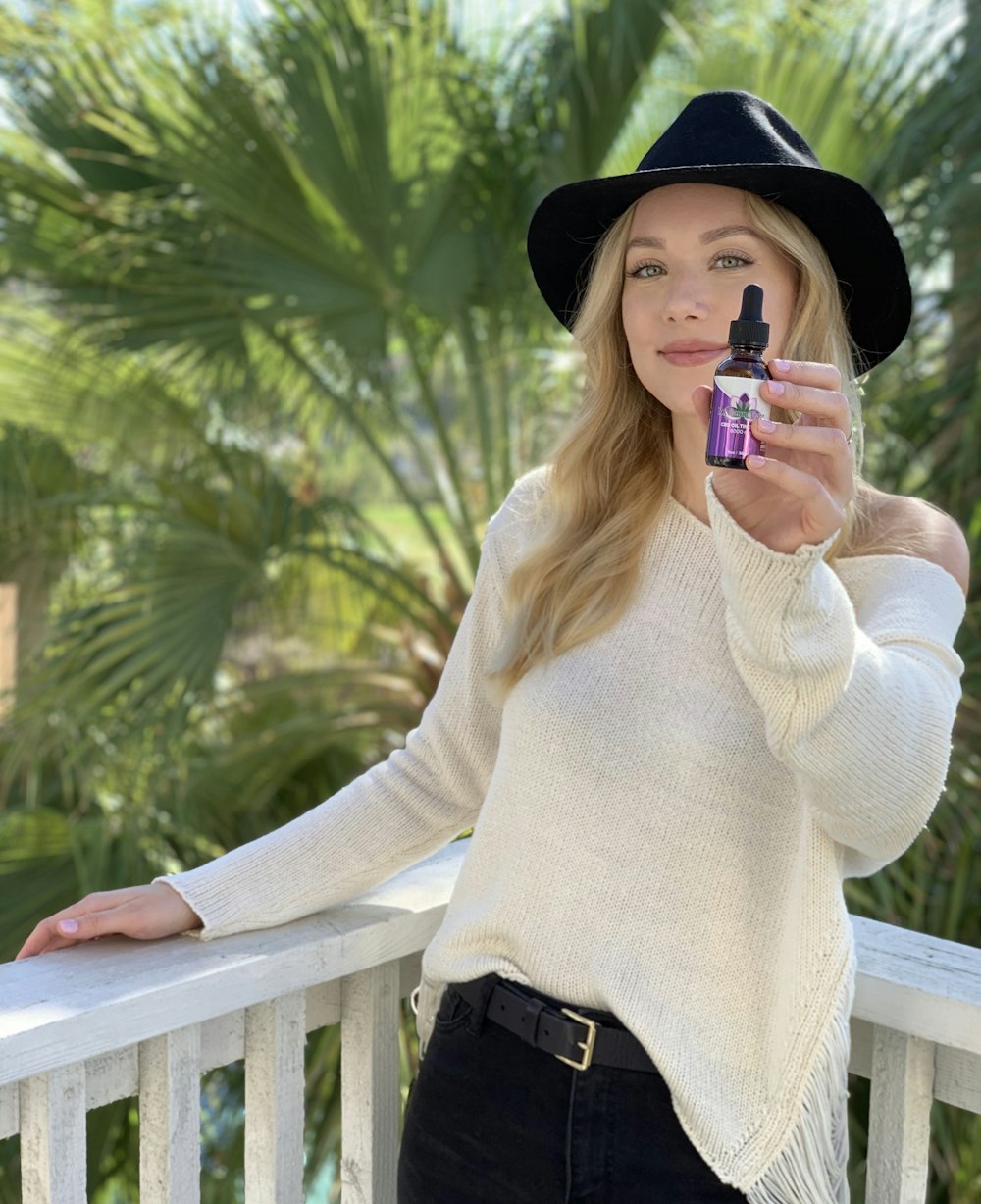 woman in white sweater and black hat holding a disposable cup