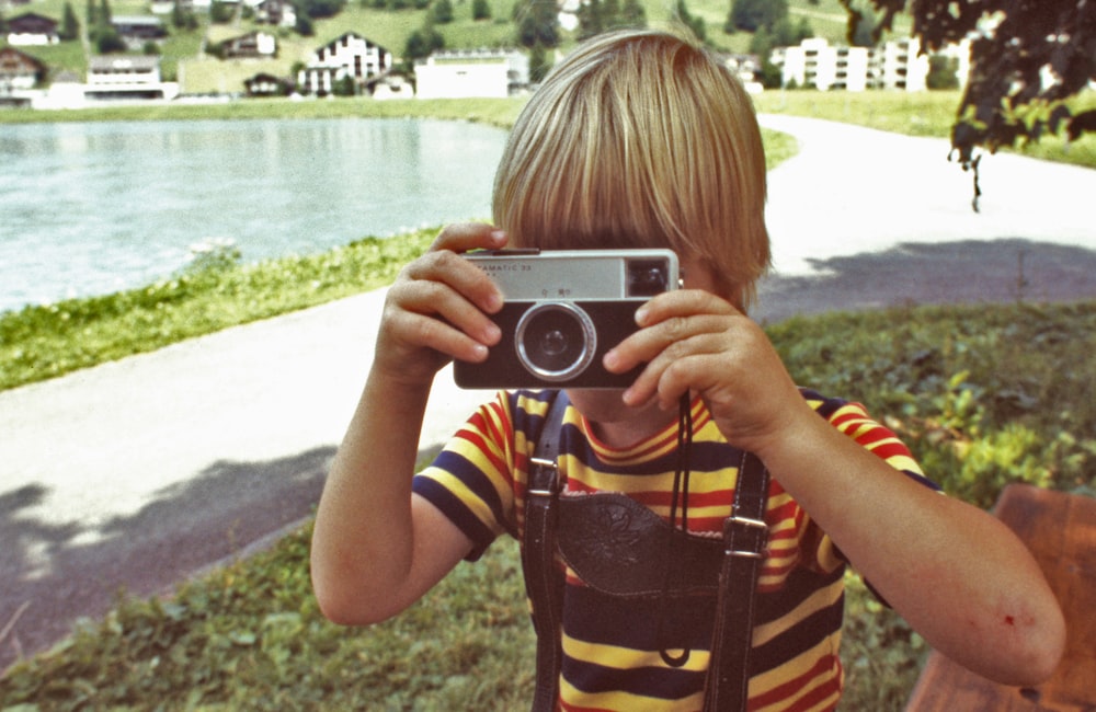 girl in yellow and black stripe shirt holding gray and black camera