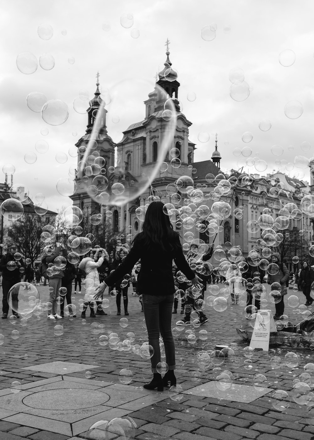 grayscale photo of woman in black jacket and pants standing on street with bubbles