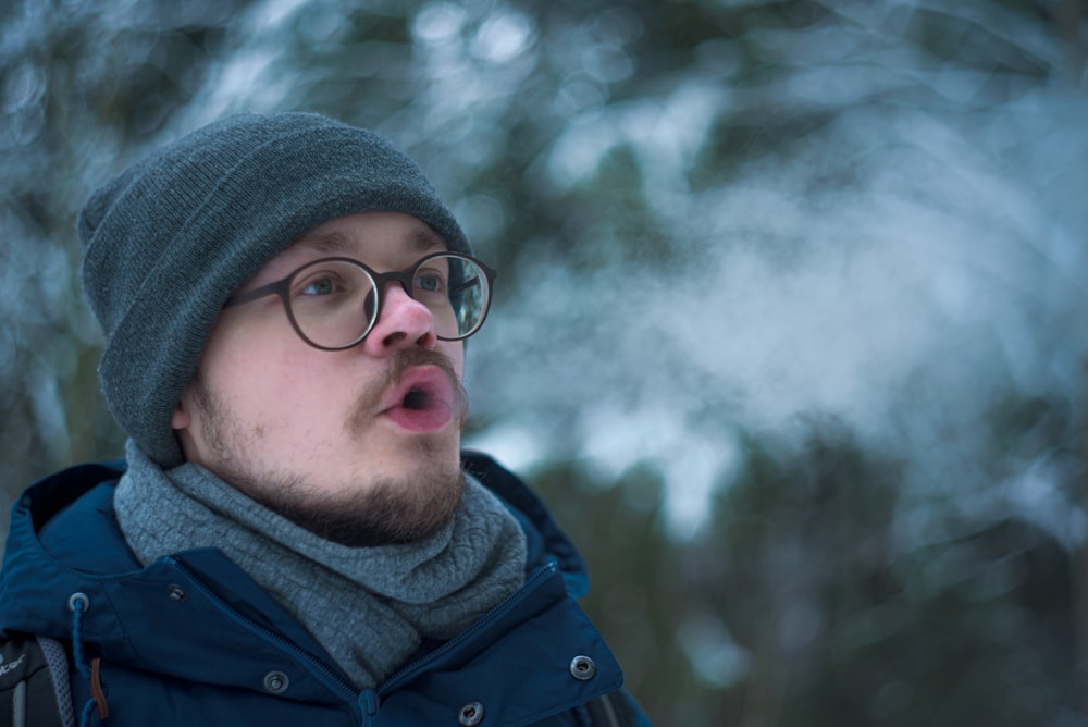 man in blue jacket wearing gray knit cap and black framed eyeglasses