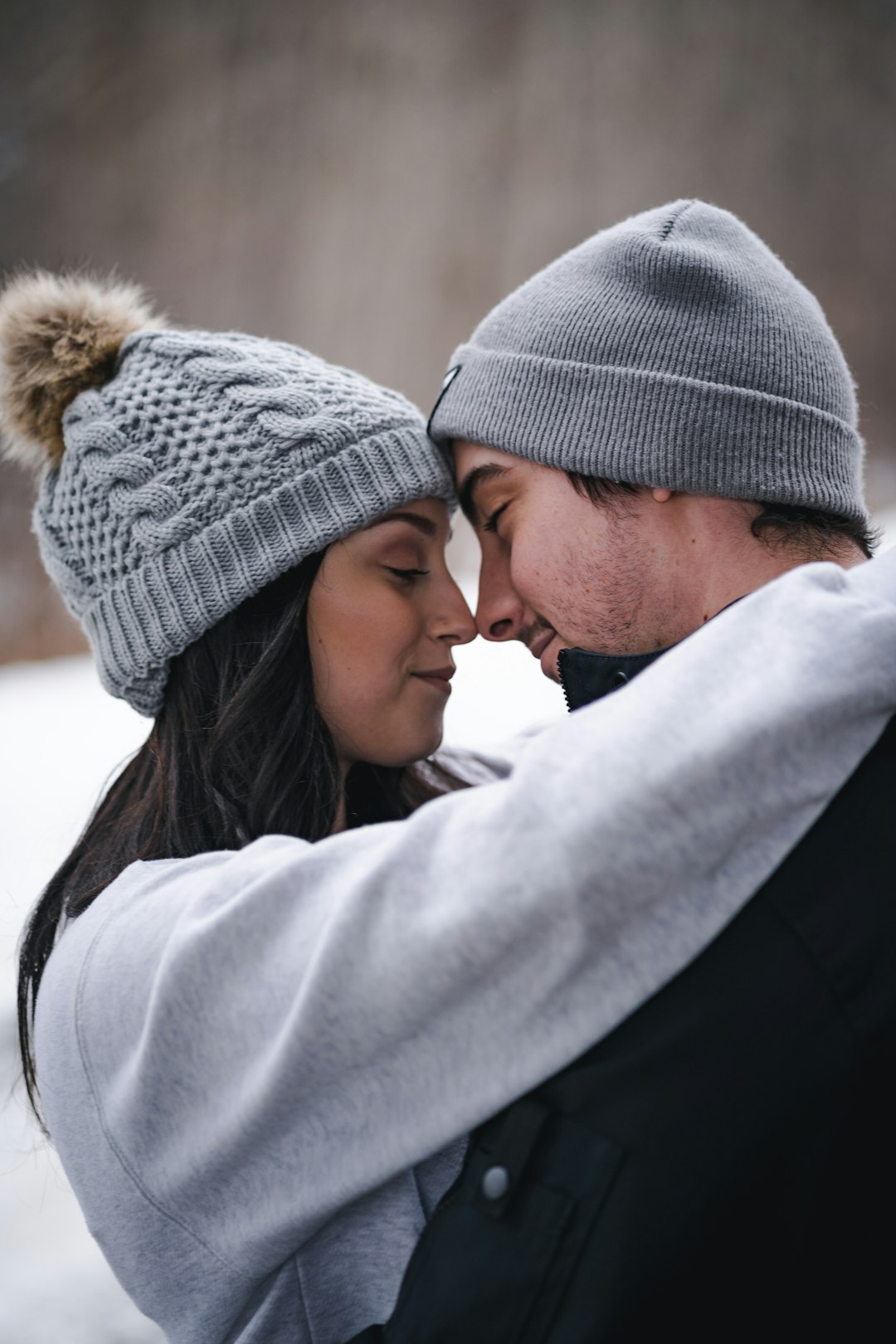 man in black knit cap kissing woman in white coat
