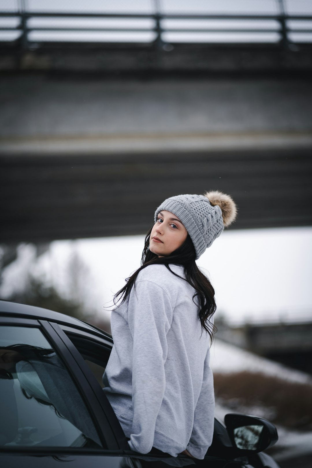 woman in white knit cap and white coat standing beside black car during daytime