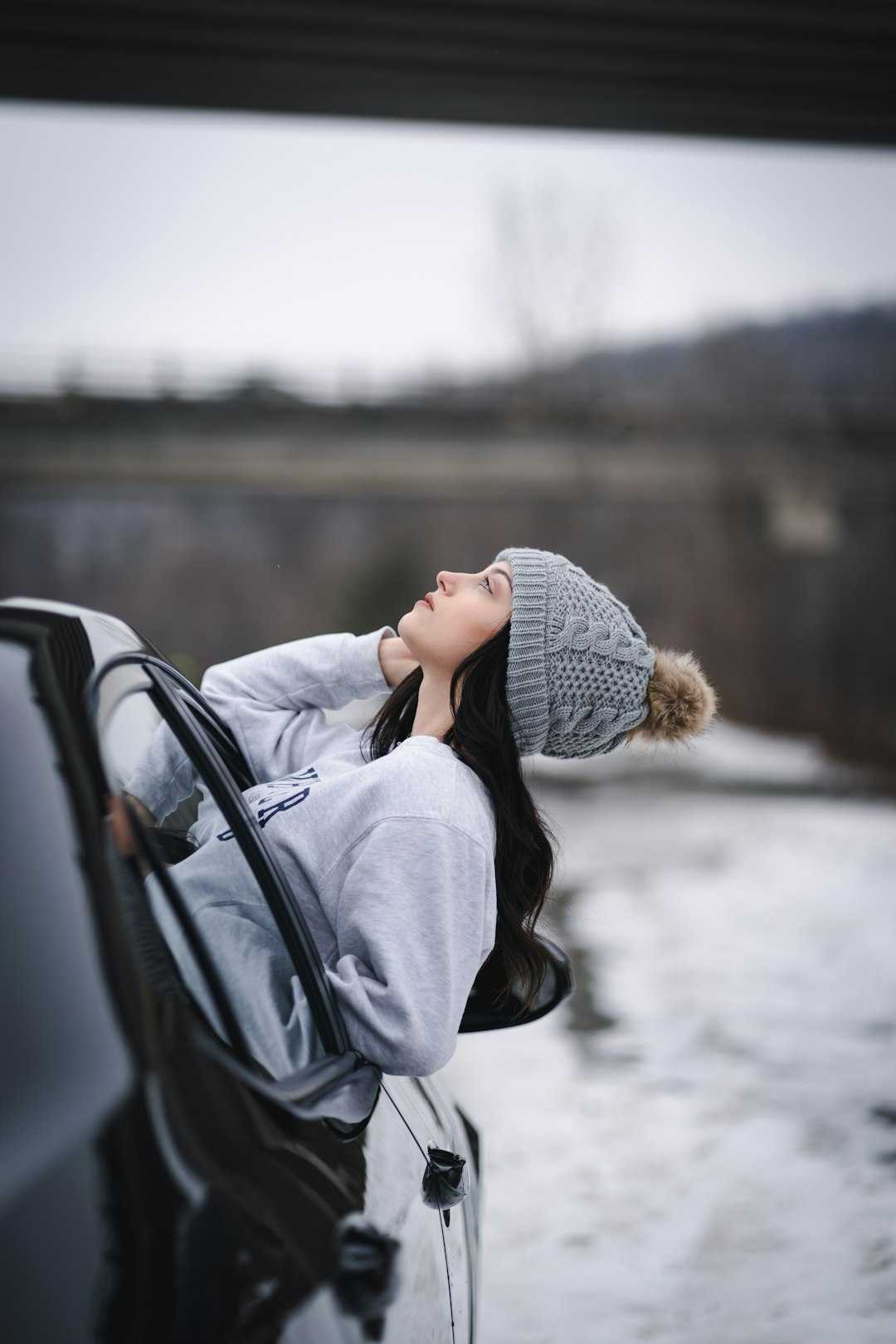 woman in gray knit cap and gray jacket leaning on black car during daytime