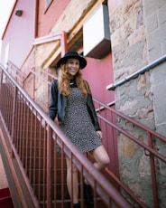 woman in black and white polka dot dress and black hat standing on stairs