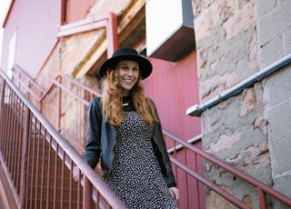 woman in black and white polka dot dress and black hat standing on stairs