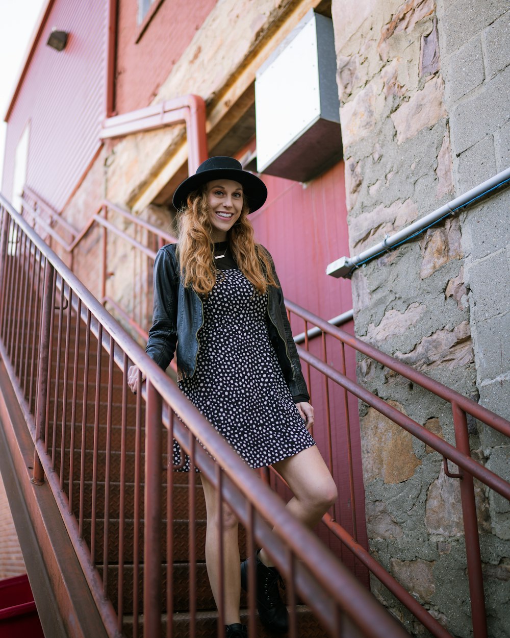 woman in black and white polka dot dress and black hat standing on stairs