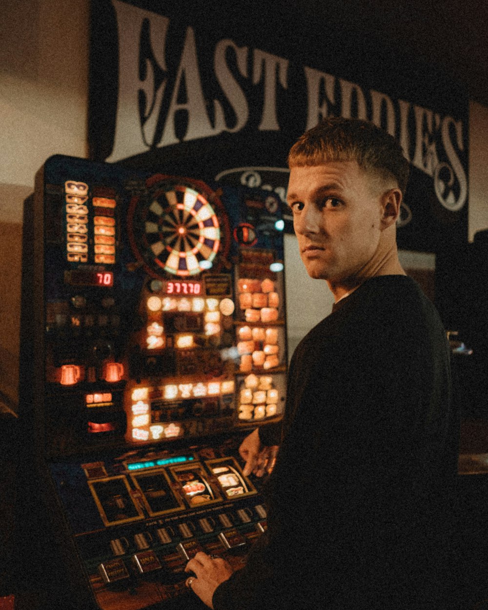 homme en chemise noire debout près de la machine d’arcade noire et rouge