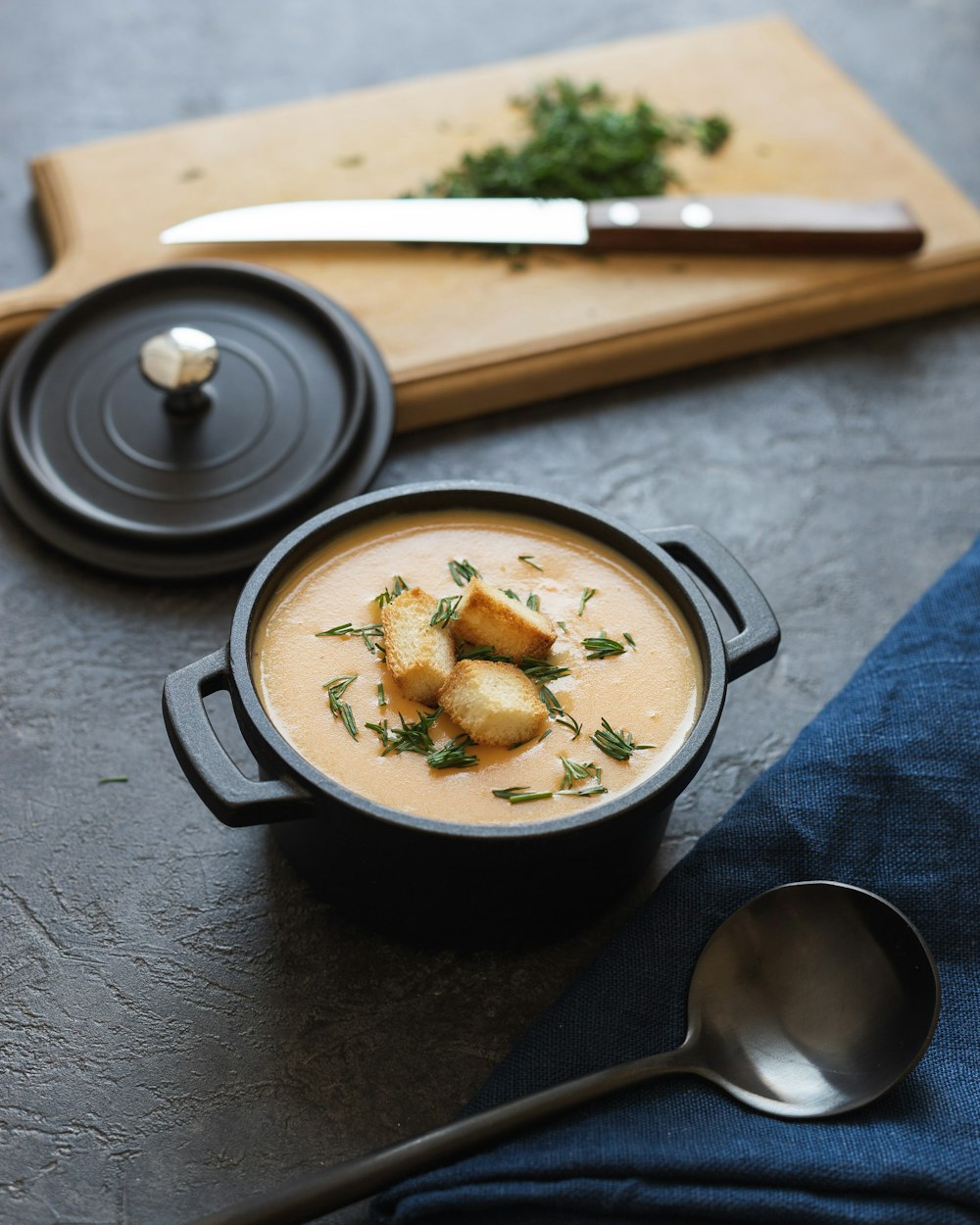 schwarze Keramikschüssel mit Suppe neben Edelstahllöffel